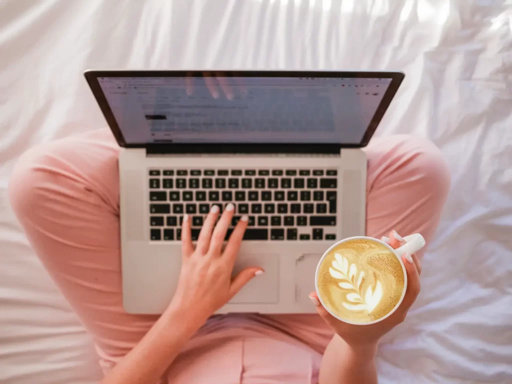 mulher tomando café e pesquisando como divulgar seu trabalho nas redes sociais usando um notebook